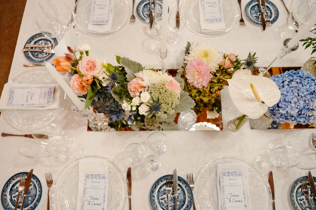 My Pretty Vintage Wedding Décor and Floral Stylist & Wedding Hire. Guest Table with Chrystal Chandeliers, White and Blue Delft Dinnerware and Menus with Colourful Flowers